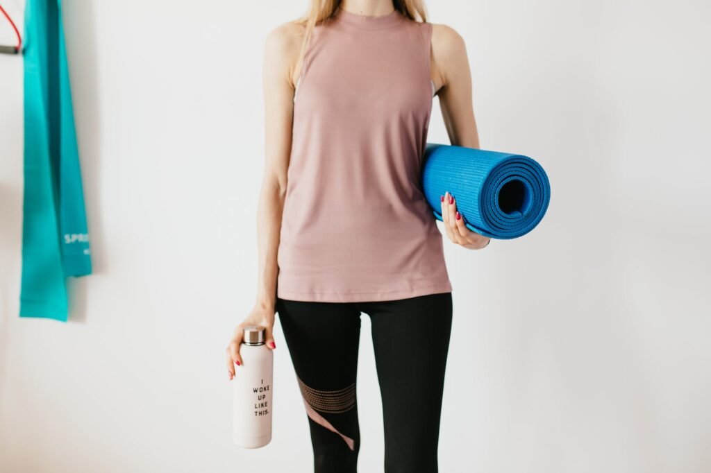 crop sportswoman carrying sport mat and bottle of water before exercising - staying hydrated